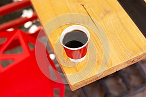 A wooden table on which there is a red plastic cup with coffee. Summer beautiful terrace in greenery. Cozy place