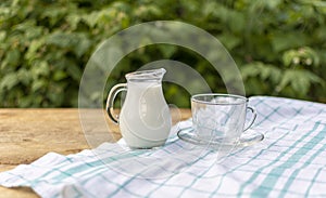 On a wooden table with a white tablecloth is a glass jug of milk