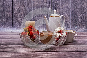 Two vases with strawberries, two glasses with cocktail, up of coffee, teapot stand on wooden table.