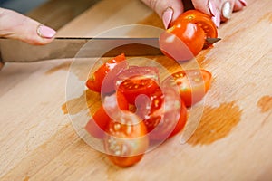 On a wooden table, a woman knifes a regimen of cherry tomatoes on slices for vegetable salad