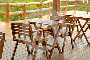 Wooden tables and chairs at outdoor cafe terrace in park. Empty garden furniture surrounded by green garden