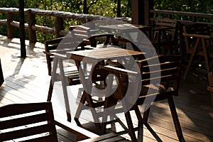 Wooden tables and chairs at outdoor cafe terrace in park. Empty garden furniture surrounded by green garden