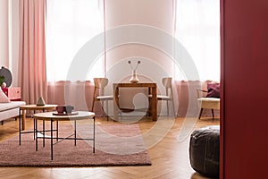 Wooden tables on purple carpet in living room interior with pink drapes at window. Real photo