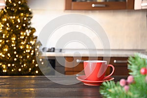 Wooden tabletop with red cup of coffee and blurred Christmas kitchen