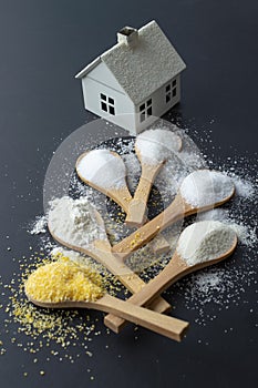 Wooden teaspoons with flour, salt, sugar, semolina, and corn flour, leading to a miniature metal home