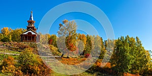 Wooden temple on Lake Baikal in the yellow trees of the autumn forest. Panorama Russia