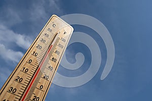 Wooden thermometer with red measuring liquid showing high temperature over 32 degrees Celsius on background of blue sky