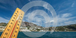 Wooden thermometer with red measuring liquid showing high temperatures on sunny day on background of seaside.