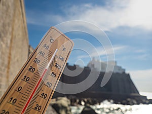 Wooden thermometer with red measuring liquid showing high temperatures on sunny day on background of seaside.