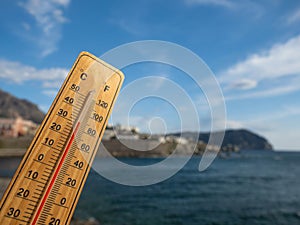 Wooden thermometer with red measuring liquid showing high temperatures on sunny day on background of seaside.