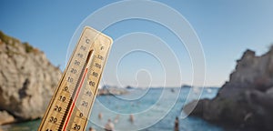 Wooden thermometer with red measuring liquid showing high temperatures on sunny day on background of seaside.