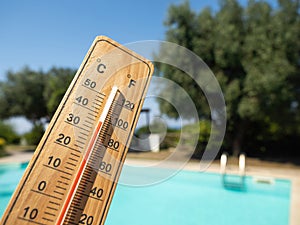 Wooden thermometer with red measuring liquid showing high temperatures on sunny day on background of swimming pool.