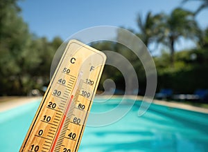 Wooden thermometer with red measuring liquid showing high temperatures on sunny day on background of swimming pool.