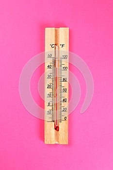 A wooden thermometer showing 30-40 degrees of heat on a pink pastel background. Summer. Top view. Flat lay. Copy space.