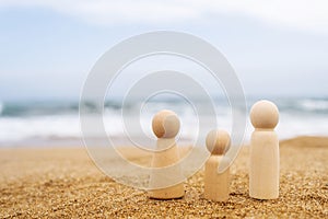 Wooden three figures of people on the sand of beach with sea view. Concept of happy family with two kids on holiday.