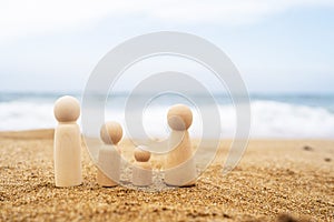 Wooden three figures of people on the sand of beach with sea view. Concept of happy family with two kids on holiday.