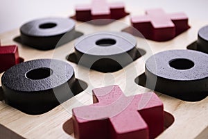 Wooden tic tac toe game on white background. Red crosses and black noughts. Macro