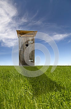 Wooden toilet, green field, blue sky