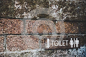 A wooden toilet sign on the old brick wall.