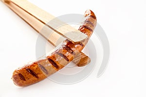 Wooden tongs holding a cooked, seared sausage