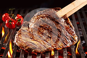 Wooden tongs picking up beef on grill