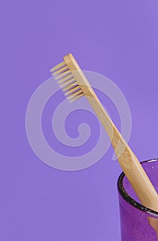 Wooden toothbrush in a glass on a purple background