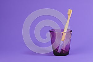 Wooden toothbrush in a glass on a purple background