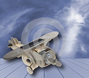 Wooden toy airplane with solar panel on blue wood, on blue sky and cloud background