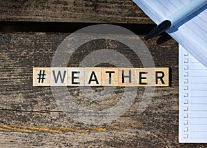 Wooden toy blocks with the text weather on it with pen and paper in the background