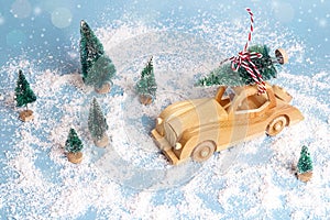 Wooden toy car with Christmas tree on the roof on blue snow back