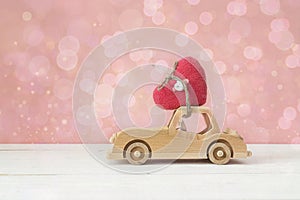 Wooden toy car with heart on the roof on a pink background. Place for text.