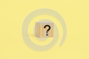 wooden toy cube with a question mark viewed high angle on a yelllow background with copy space
