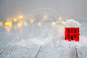 Wooden toy house in a snow and light boche on a wooden background