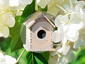 Wooden toy house in the white hydrangea flowers against the green background