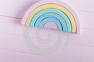 Wooden toy rainbow, pastel color arc on light pink background. Natural no plastic toys for creativity development.