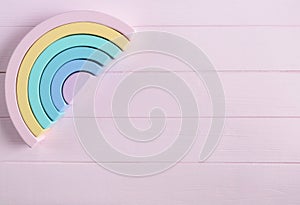 Wooden toy rainbow, pastel color arc on light pink background. Natural no plastic toys for creativity development.