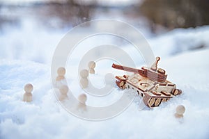 A wooden toy Russian tank T-34 and little men in the snow. Russia and Ukraine are at war in winter. Encirclement photo
