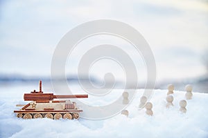 A wooden toy Russian tank T-34 and little men in the snow. Russia and Ukraine are at war in winter. Encirclement photo