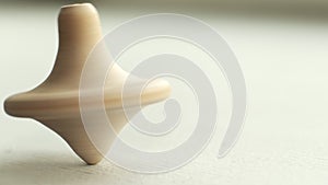 wooden toy spinning top is spinning on a white table. The top slows down, losing balance or stability and falls on its