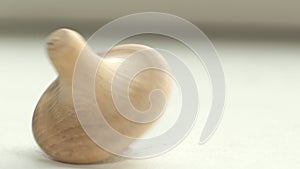 wooden toy spinning top is spinning on a white table. The top slows down, losing balance or stability and falls on its