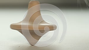 wooden toy spinning top is spinning on a white table. The top slows down, losing balance or stability and falls on its