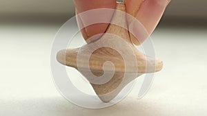 wooden toy spinning top is spinning on a white table. The top slows down, losing balance or stability and falls on its