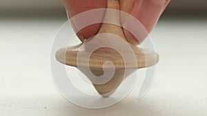 Wooden toy spinning top is spinning on a white table. The top slows down, losing balance or stability and falls on its