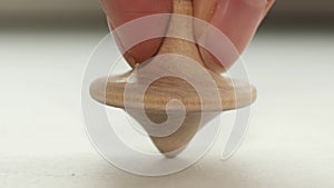 wooden toy spinning top is spinning on a white table. The top slows down, losing balance or stability and falls on its