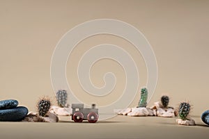 Wooden toy steam locomotive in desert with stones and cactuses on beige backdrop