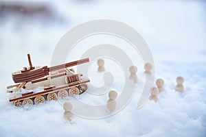 A wooden toy tank and little men in the snow. Russia and Ukraine are at war in winter. Encirclement, retreat, attack