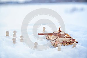 A wooden toy tank and little men in the snow. Russia and Ukraine are at war in winter. Encirclement, retreat, attack