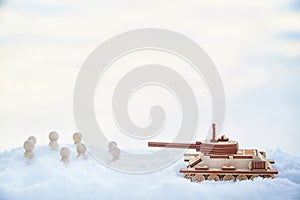 A wooden toy tank and little men in the snow. Russia and Ukraine are at war in winter. Encirclement, retreat, attack photo