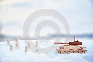 A wooden toy tank and little men in the snow. Russia and Ukraine are at war in winter. Encirclement, retreat, attack photo