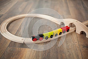 Wooden toy train on railroad with wooden bridge. Clean laminated floor